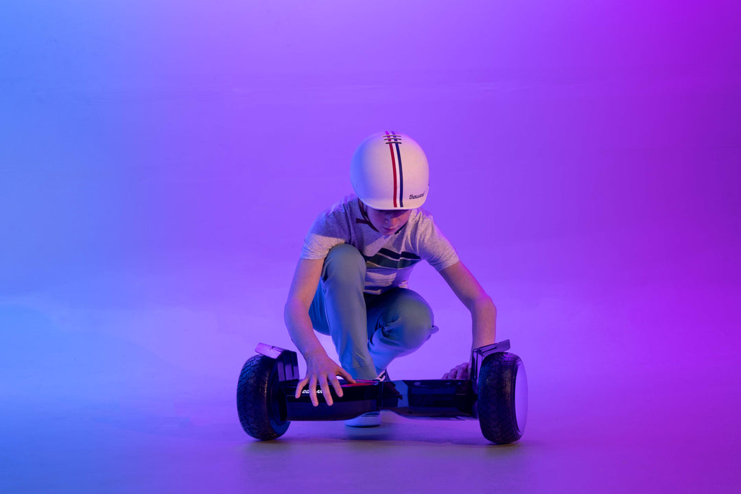Child preparing to ride GOTRAX E5 Off-Road Bluetooth Hoverboard with Infinity Wheels wearing a Thousand Brand Speedway Creme Helmet